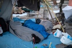 A dog sits next to migrants as they sleep on a road leading from Moria to the capital of Mytilene, on the northeastern island of Lesbos, Greece, Sept. 17, 2020.