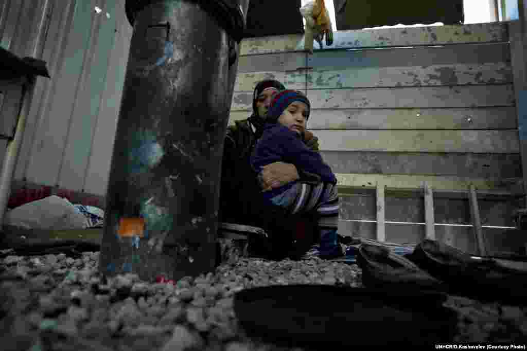 Seorang ibu Suriah memeluk cucunya dekat kompor di depan rumah kontainer mereka di kamp pengungsi di Harmanli. UNHCR/D.Kashavelov