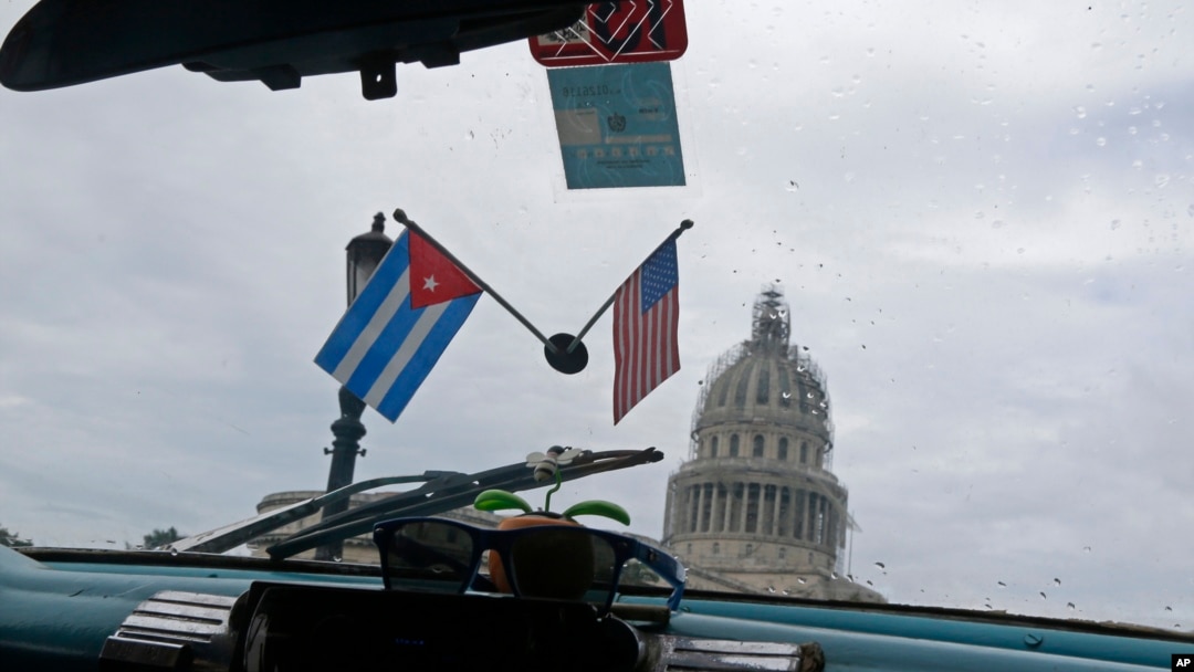 Miniatur bendera nasional Kuba dan Amerika Serikat menghiasi sebuah taksi yang melewati Gedung Capitol di Havana, Kuba. (Foto: Dok)