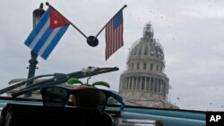 Banderas de Cuba y Estados Unidos decoran el interior de un automóvil estadounidense clásico utilizado como taxi que pasa por el Capitolio de La Habana, Cuba, el viernes 16 de enero de 2015.