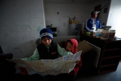 In this July 10, 2019, photo, Nahum Perla studies a map with his younger brother, Carlos Isai Perla, as their father, Juan Carlos Perla, right, gets ready to make the journey from their home in Tijuana, Mexico, to San Diego for an asylum hearing.