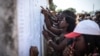 Youth check lists of names to see if they were selected as poll workers for the upcoming general elections in Port Loko, Sierra Leone, March 3, 2018. Youth unemployment is a chronic challenge in the West African nation. (J. Patinkin/VOA)