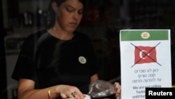 FILE - An employee stands behind a sign depicting a crossed out Turkish flag taped to the window of a coffee shop in Tel Aviv, Oct. 27, 2009. 