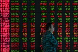 In this Sept. 19, 2019, photo, a man walks by an electronic board displaying stock prices at a brokerage house in Beijing.