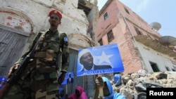 Wani sojan gwamnatin Somaliya yana wucewa a kusa da wata mace rike da kwalin fasta na yakin neman zaben shugaba Sheikh Sharif Ahmed