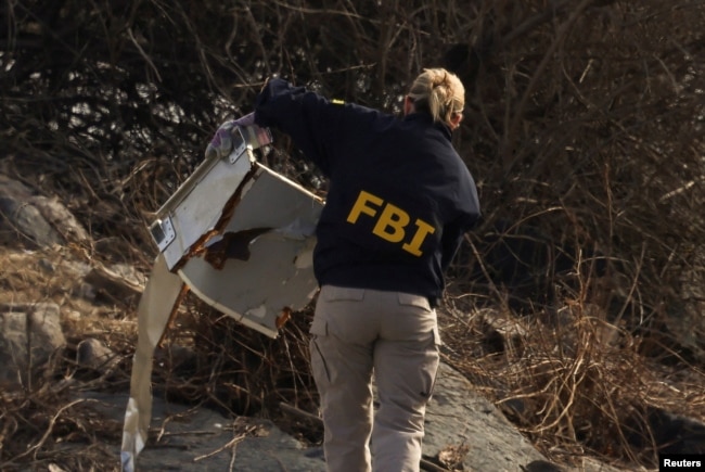 An FBI agent carries debris after an American Airlines flight, operated by affiliate PSA Airlines, collided with a Black Hawk helicopter while approaching Ronald Reagan Washington National Airport and crashed into Potomac River, in Arlington, Virginia, Jan. 30, 2025.