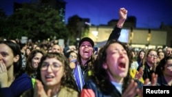 Várias pessoas assistem à cobertura da libertação de Romi Gonen, Doron Steinbrecher e Emily Damari.