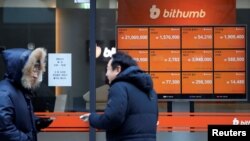 Men talk in front of an electric board showing exchange rates of various cryptocurrencies at Bithumb cryptocurrencies exchange in Seoul, South Korea, Jan. 11, 2018.