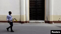 FILE - A woman walks past closed doors at the Church of Our Virgin of Charity in Havana March 14, 2012.