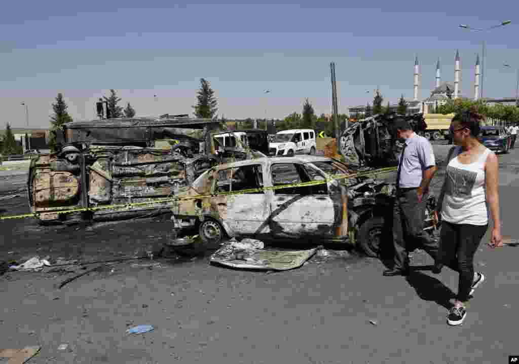 Turkish citizens walk past burnt and destroyed police and civilian vehicles near the presidential palace, in Ankara, July 17, 2016, that were attacked by a Turkish airstrike during a military coup late Friday.