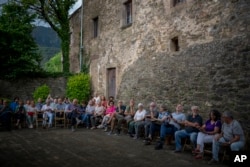 Villagers of Joanetes, Spain sit next to the 12th-century Sant Romà church as the students of the Vall d'en Bas School of Bell Ringers play its bells on Saturday, June 29, 2024. (AP Photo/Emilio Morenatti)