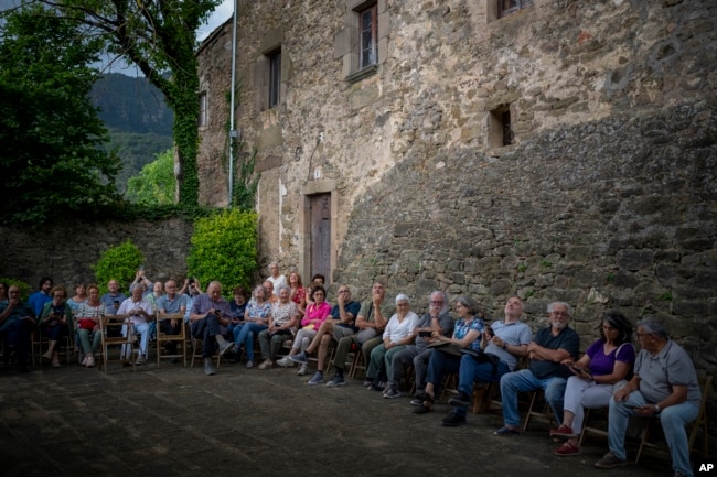 Villagers of Joanetes, Spain sit next to the 12th-century Sant Romà church as the students of the Vall d'en Bas School of Bell Ringers play its bells on Saturday, June 29, 2024. (AP Photo/Emilio Morenatti)