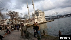 Couples pose for souvenir pictures in front of the Ottoman-era Ortakoy Mecidiye mosque by the Bosphorus strait in Istanbul, Turkey, Jan. 5, 2015. 