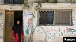 FILE - A Palestinian refugee woman living in Jordan wears a traditional Palestinian dress as she poses in front of her home at Al-Baqaa Palestinian refugee camp, near Amman, Jordan, June 16, 2020.