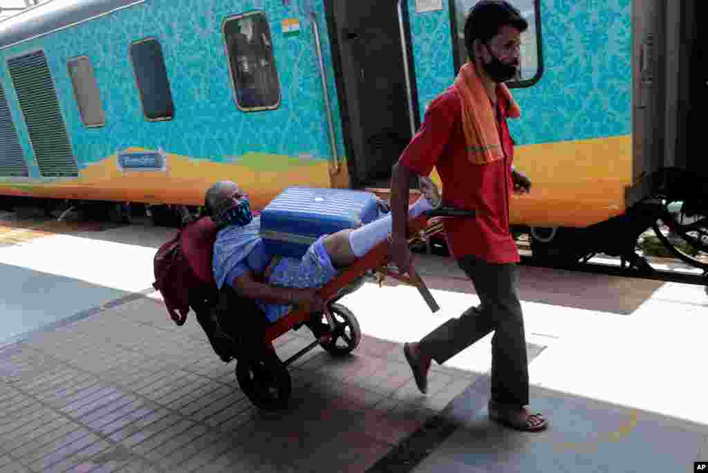 A railway porter transports an elderly passenger who has difficulties in walking, on a baggage trolley to a train in Mumbai, India.