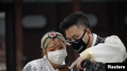 FILE - A couple wearing masks to prevent contacting the coronavirus looks at a mobile phone at Gyeongbok Palace in central Seoul, South Korea, March 1, 2020.