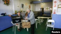 A man receives his voting paper from poll clerks in a public launderette being used as a polling station in Oxford, May 7, 2015.