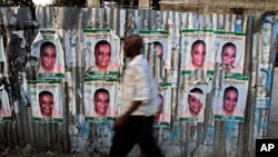 A man walks past a corrugated fence covered with election posters in Port-au-Prince (file - March 16, 2011)