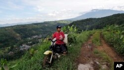 Seorang petani mengendarai sepeda motor di jalan berlumpur dengan pemandangan Gunung Gede Pangrango, Maret 2018. Kawasan dekat Gunung Gede akan menjadi lokasi proyek patungan antara perusahaan milik Presiden AS Donald Trump dan MNC Land, milik Hary Tanoesoedibjo. (AP Photo/Tatan Syuflana)