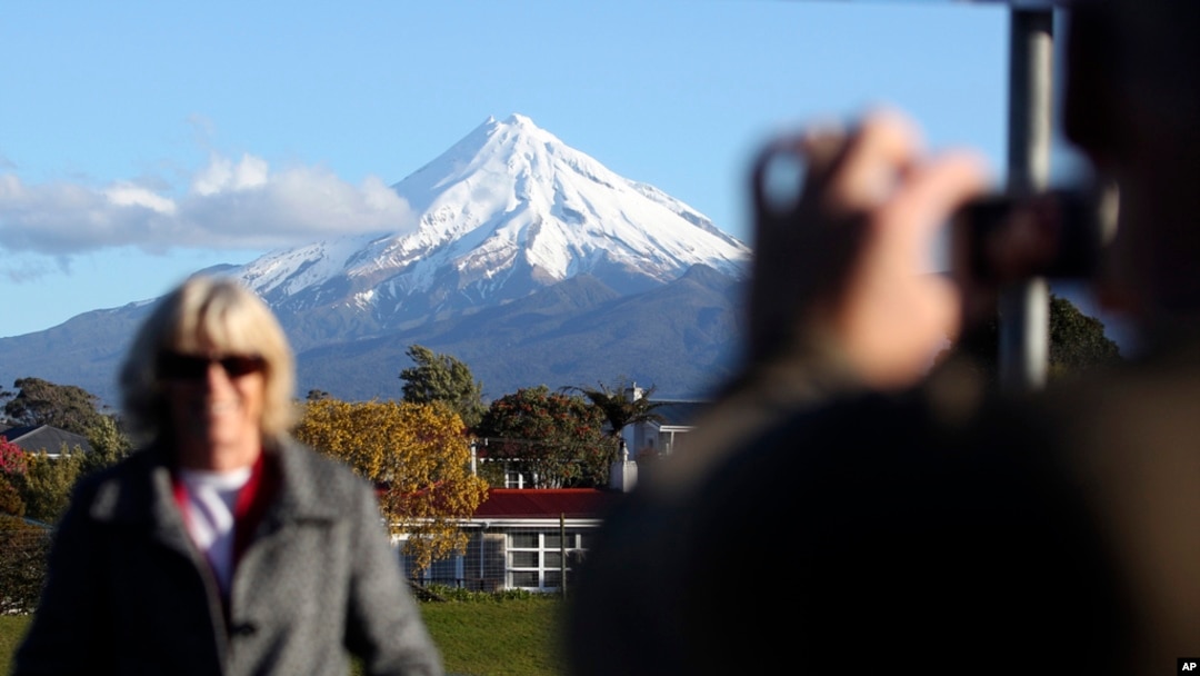 FILE - A man takes a picture of his wife with Taranaki Maunga, previously known as Mount Taranaki, in the background in New Plymouth, New Zealand, Sept. 26, 2011.