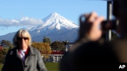 FILE - A man takes a picture of his wife with Taranaki Maunga, previously known as Mount Taranaki, in the background in New Plymouth, New Zealand, Sept. 26, 2011.