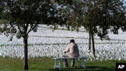 FILE - A visitor sits on a bench to look at artist Suzanne Brennan Firstenberg's "In America: Remember," a temporary art installation made up of white flags to commemorate Americans who have died of COVID-19, on the National Mall in Washington on Oct. 2, 2021. 