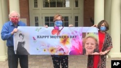 This May 3, 2020, photo by Shelly Solomon shows, from left, Steve Turner and his sisters, Carla Paull and Lisa Fishman, holding up a Mother’s Day banner with images of their mom, Beverly Turner, outside her assisted living facility in Ladue, Missouri.