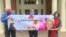 This May 3, 2020, photo by Shelly Solomon shows, from left, Steve Turner and his sisters, Carla Paull and Lisa Fishman, holding up a Mother’s Day banner with images of their mom, Beverly Turner, outside her assisted living facility in Ladue, Missouri.