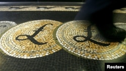 FILE - An employee is seen walking over a mosaic of pound sterling symbols set in the floor of the front hall of the Bank of England in London, Britain.