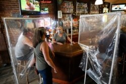 Sheila Kelly, center, owner of Powell's Steamer Co. & Pub, stands behind makeshift barriers as she helps patrons at her restaurant in the El Dorado County town of Placerville, Calif., May 13, 2020.