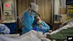 FILE - A woman, center, is comforted by a nurse, left, as she weeps while sitting at the bedside of her dying husband, in St. Jude Medical Center's COVID-19 unit in Fullerton, California, July 31, 2020.