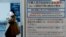 日本東京羽田機場一名戴著口罩的女子走過武漢肺炎的防疫廣告牌。（2020年1月20日）