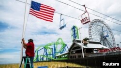 Seorang pekerja mengibarkan bendera AS di pantai Seaside Heights setelah pantai-pantai di New Jersey dibuka kembali menjelang peringatan Hari Pahlawan atau Memorial Day di tengah pandemi virus corona, Seaside Heights, New Jersey, 23 Mei 2020. (Foto: Reuters)