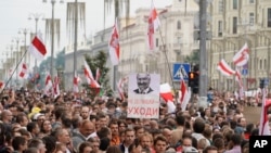 FILE - Belarusian opposition supporters carry old Belarusian flags and a poster with a portrait of Belarusian President Alexander Lukashenko reading "Go away," at a rally at Independence Square in Minsk, Belarus, Aug. 23, 2020. 