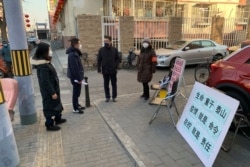 People in face masks stand near a stall to register residents who have recently returned from other provinces in a neighborhood in Beijing, Jan. 31, 2020.