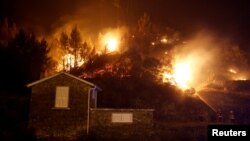 Firefighters work to save a house from a forest fire in Carvalho, near Gois, Portugal, June 19, 2017. 