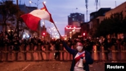 A protestor waves a Peruvian flag as police officers stand guard during a protest demanding the dissolution of Congress and to hold democratic elections rather than recognize Dina Boluarte as Peru's President, in Lima, Peru Dec. 11, 2022. 