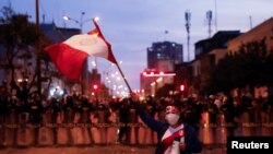 Un manifestante ondea una bandera peruana mientras los policías hacen guardia durante una protesta que exige la disolución del Congreso y la celebración de elecciones democráticas en lugar de reconocer a Dina Boluarte como presidenta de Perú, luego de la destitución del líder peruano Pedro Castillo, en Lima, Perú, 11 de diciembre de 2022 REUTERS/Alessandro Cinque