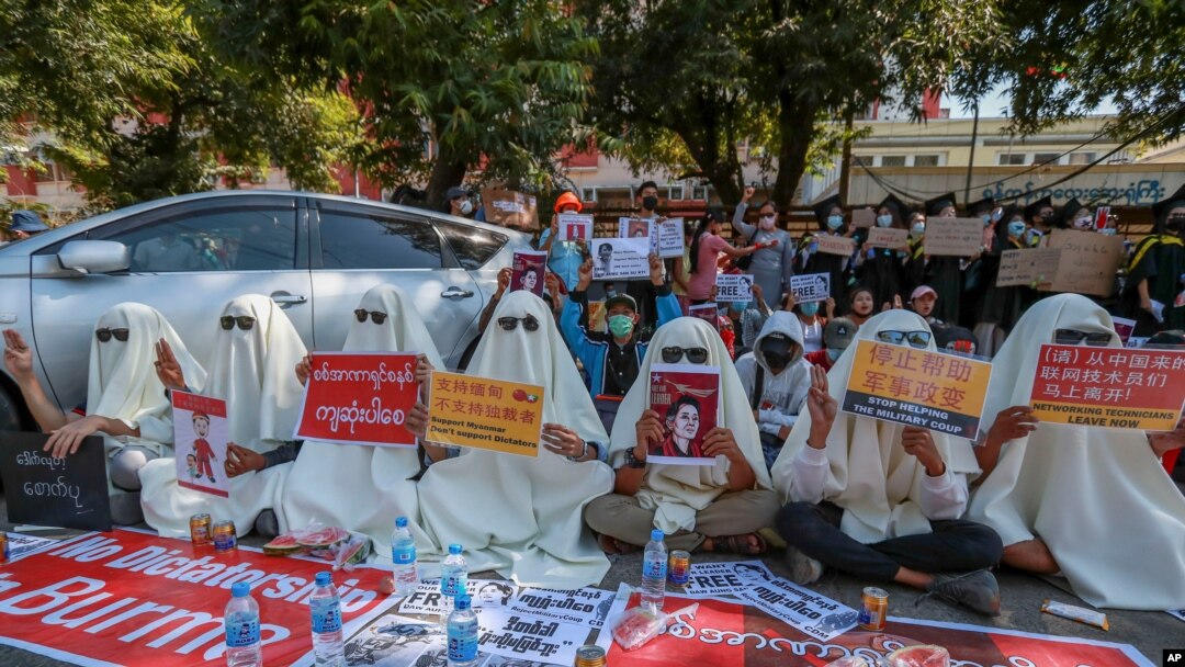 FILE - Hooded demonstrators display placards accusing China of supporting Myanmar's military during a protest against the recent coup, outside the Chinese Embassy in Yangon, Myanmar, Feb. 11, 2021.