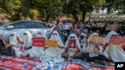 FILE - Hooded demonstrators display placards accusing China of supporting Myanmar's military during a protest against the recent coup, outside the Chinese Embassy in Yangon, Myanmar, Feb. 11, 2021.