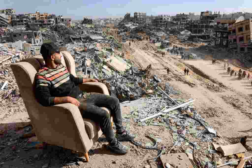 A man sits on a lounge chair atop a heavily-damaged building along Saftawi street in Jabalia in the northern Gaza Strip, a day after a ceasefire deal in the war between Israel and Hamas went into effect.