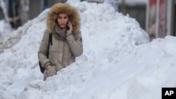 FILE - A woman waits between large piles of snow at a bus stop in Bucharest, Romania, Jan. 11, 2017. A study in Romania says snow has a freshness date, of sorts, for consumption.