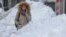 FILE - A woman waits between large piles of snow at a bus stop in Bucharest, Romania, Jan. 11, 2017. A study in Romania says snow has a freshness date, of sorts, for consumption.