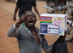 A man reacts while carrying a bag of noodles during a mass looting of a warehouse that have COVID-19 food palliatives that were not given during lockdown to relieve people of hunger, in Abuja, Nigeria, Oct. 26, 2020.