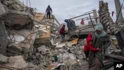 Fatima Rehan carries her 2-year-old son Mohammed as she and other members of the Rehan family search the rubble of their home destroyed by the Israeli army's air and ground offensive against Hamas in Jabaliya, Gaza Strip, Feb. 5, 2025. 