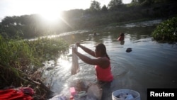 Una solicitante de asilo lava su ropa en el río Bravo mientras espera intentar cruzar a los EE. UU. con una cita a través de la aplicación de Aduanas y Protección Fronteriza, llamada CBP One, en un campamento improvisado en Matamoros, México, el 21 de junio de 2023.