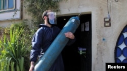 FILE - A volunteer carries an oxygen cylinder, to be delivered to a patient suffering from the coronavirus disease and receiving home care, in Damascus, Syria, March 3, 2021. 