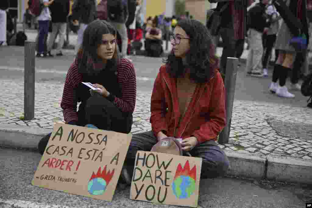 Dos jóvenes manifestantes se sientan en el suelo con carteles que citan a la activista climática sueca Greta Thunberg, en Lisboa, durante una protesta mundial que exige una acción sobre el cambio climático, el viernes 29 de noviembre de 2019. Se espera que Thunberg llegue a Lisboa en los próximos días antes de dirigirse a la conferencia climática COP 25 en Madrid. El cartel a la izquierda dice en portugués: &quot;Nuestra casa está en llamas&quot;.