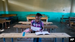 A lone student looks over papers as she waits for her teacher to arrive at the Lycée school, which reopened about a week earlier than other schools in Petion-Ville, Haiti, Nov. 28, 2019. 