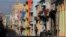 FILE - A man pushes his motorcycle as people walk on the freshly painted buildings along Reina Street in Havana, Cuba, Sept. 19, 2015. 